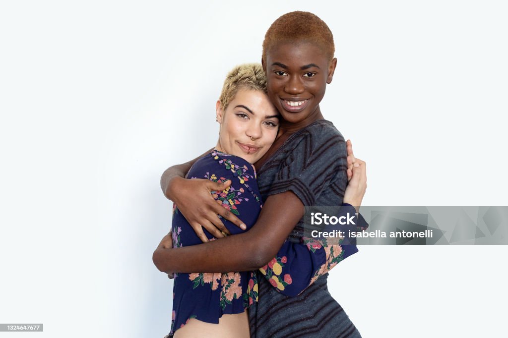 Photo of joyful ladies embrace and enjoy togetherness, being of different of races, dressed in casual jumpers, isolated over white background Photo of joyful ladies embrace and enjoy togetherness, being of different of races, dressed in casual jumpers, isolated over white background. Diverse women laugh happily, have fun together. Lesbian Stock Photo
