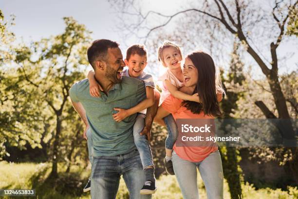 Happy Parents Having Fun While Piggybacking Their Small Kids In Nature Stockfoto en meer beelden van Familie
