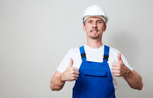 Portrait of young handyman standing on white background with copy space. Repairman wearing workwear uniform and protective hard hat