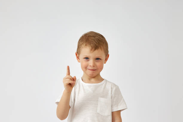 ein junge mit einem lustigen gesicht zeigt mit dem finger auf einen weißen hintergrund - moving up child pointing looking stock-fotos und bilder