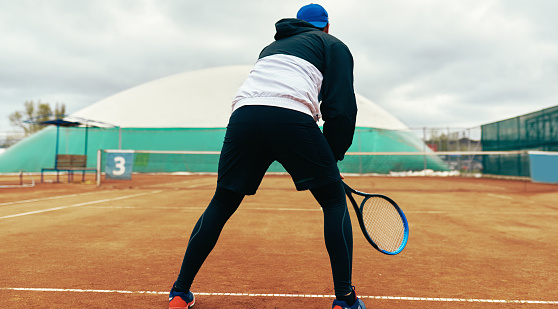 A professional male tennis player waiting to hit during a game. Young athlete man playing tennis on the court outdoors.