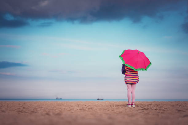 Siblings holding an umbrella watching the sea in rain