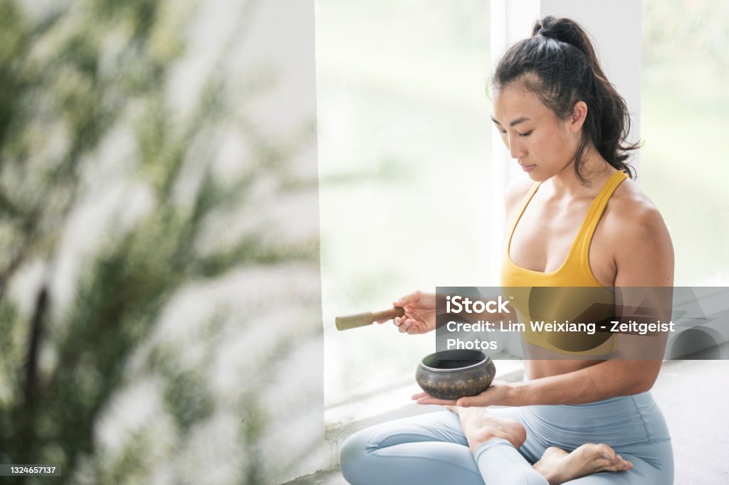 Female Asian Yogi meditating with a singing bowl Female Asian Yoga Instructor meditates with a singing bowl Rin Gong Stock Photo