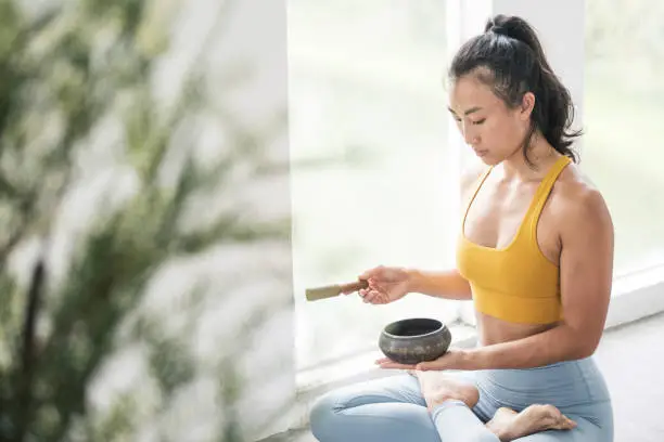 Female Asian Yoga Instructor meditates with a singing bowl