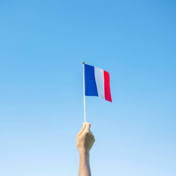 hand holding France flag on blue sky background. holiday of French National Day, Bastille Day and happy celebration concepts hand holding France flag on blue sky background. holiday of French National Day, Bastille Day and happy celebration concepts circa 14th century photos stock pictures, royalty-free photos & images