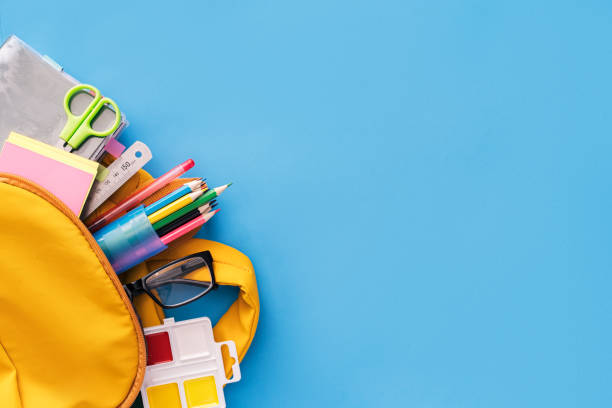 School supplies sticking out of a backpack on a blue background. Back to school concept stock photo