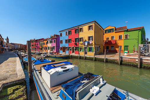 Burano island in the Venetian lagoon with beautiful multi colored houses (bright colors) and a canal with moored boats in a sunny spring day. Venice, UNESCO world heritage site, Veneto, Italy, Europe