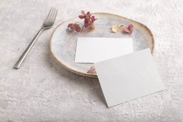 istock White paper invitation card, mockup with dried hydrangea flowers on ceramic plate and gray concrete background. Blank, side view, still life, copy space. 1324663255