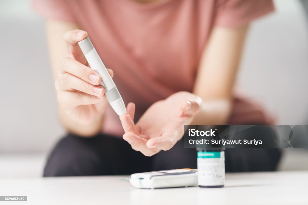Asian woman using lancet on finger for checking blood sugar level by Glucose meter, Healthcare and Medical, diabetes, glycemia concept Diabetes Stock Photo