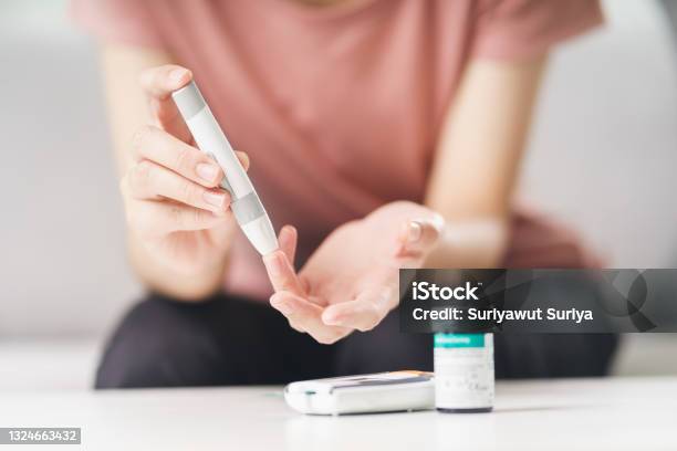 Asian Woman Using Lancet On Finger For Checking Blood Sugar Level By Glucose Meter Healthcare And Medical Diabetes Glycemia Concept Stock Photo - Download Image Now