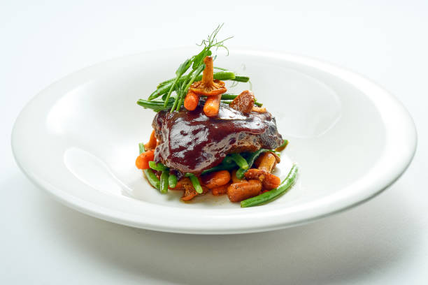 Beef cheek steak, caramelized in wine sauce with chanterelles and asparagus in a white plate. Isolated on grey background. stock photo