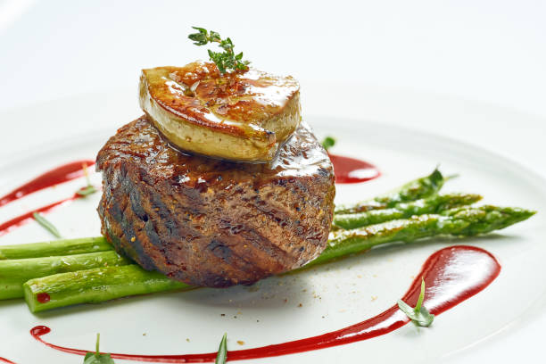 porción de bistec de mignon a la parrilla con foie gras y espárragos, salsa de bayas en un plato blanco. aislado sobre fondo gris. - comida francesa fotografías e imágenes de stock