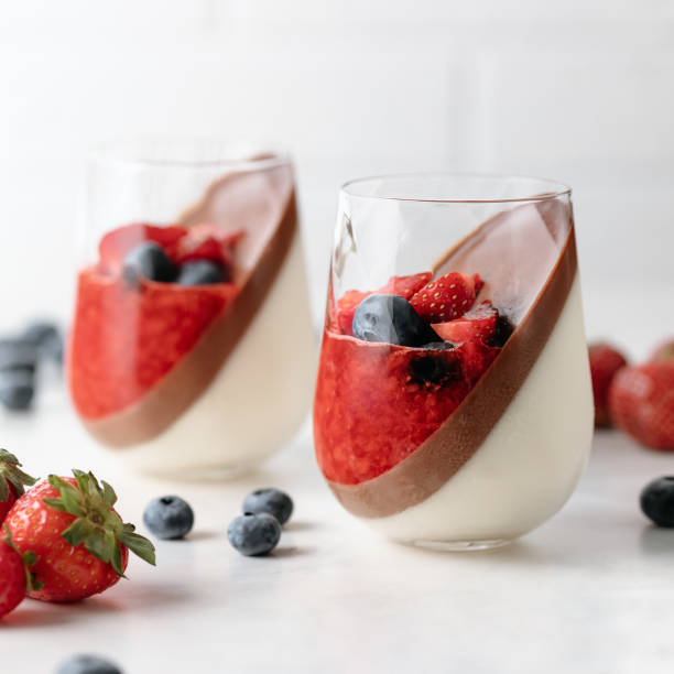 Double-layer vanilla and chocolate panna cotta dessert with with strawberry puree, fresh blueberries and strawberries  white background stock photo