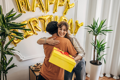 Two people, female friend bringing present to a birthday party for her male friend.
