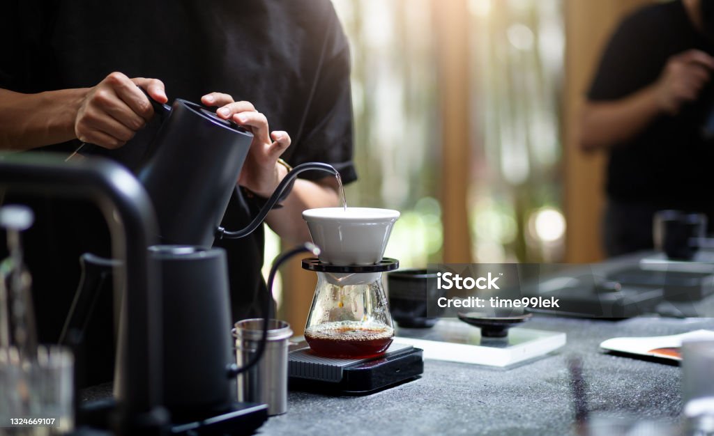 food and drink Barista pouring hot water through a coffee filter into the coffee glass on count bar in cafe Coffee - Drink Stock Photo