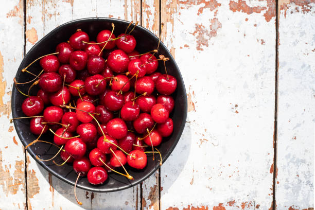 istock ripe cherries a bowl on a textured wooden background, view from above 1324673395
