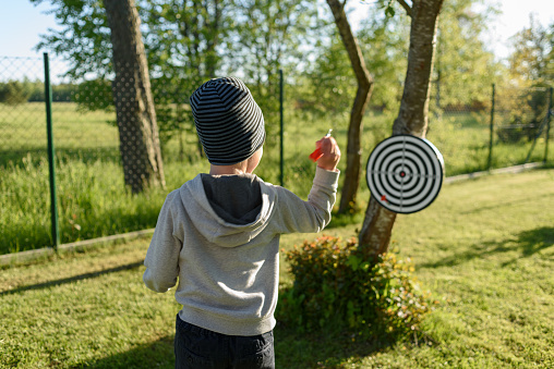 Boy playing darts at backyard, trowing arrows to target