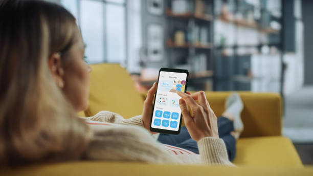 istock Beautiful Authentic Female Using a Smartphone with Food Delivery Application at Home Living Room while Lying on a Couch Sofa. She's Browsing the Catalog and Choosing, what to Order for a Dinner. 1324677929