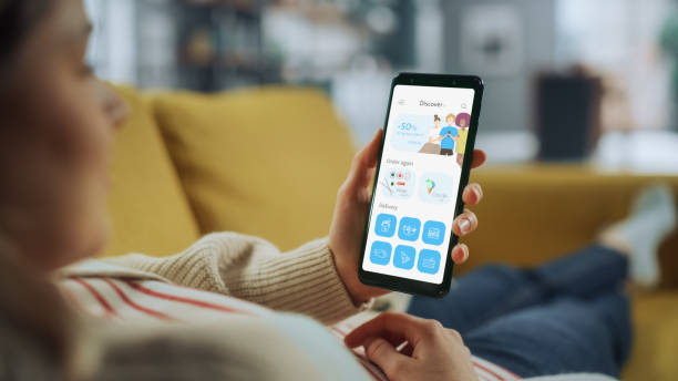 istock Beautiful Authentic Female Using a Smartphone with Food Delivery Application at Home Living Room while Lying on a Couch Sofa. She's Browsing the Catalog and Choosing, what to Order for a Dinner. 1324677933