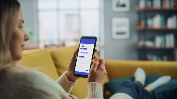 istock Beautiful Authentic Female Using a Smartphone with Calendar Application at Home Living Room while Lying on a Couch Sofa. She's Making Plans and Checking Event Schedule for a Day. 1324677991
