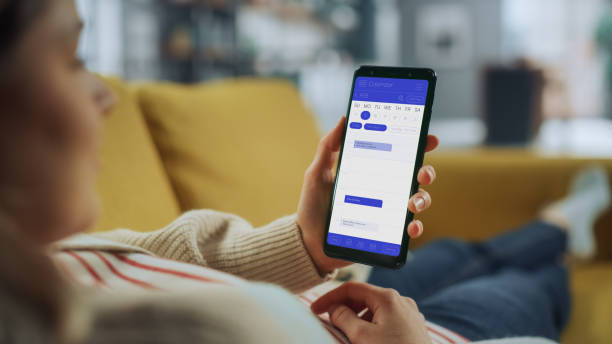 istock Beautiful Authentic Female Using a Smartphone with Calendar Application at Home Living Room while Lying on a Couch Sofa. She's Making Plans and Checking Event Schedule for a Day. 1324677993