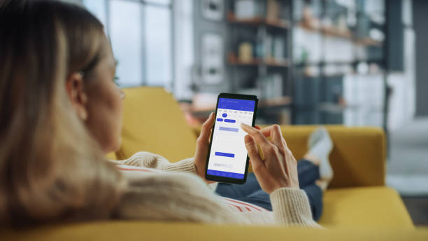 istock Beautiful Authentic Female Using a Smartphone with Calendar Application at Home Living Room while Lying on a Couch Sofa. She's Making Plans and Checking Event Schedule for a Day. 1324678002