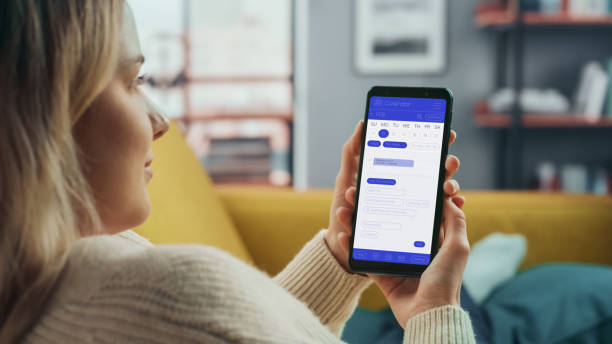 istock Beautiful Authentic Female Using a Smartphone with Calendar Application at Home Living Room while Lying on a Couch Sofa. She's Making Plans and Checking Event Schedule for a Day. 1324678039
