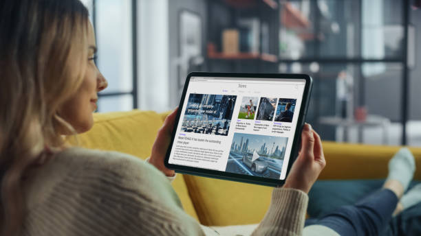istock Beautiful Authentic Female Using Tablet Computer for Reading Latest News and Articles about Technology. She is Lying on a Couch at Home Living Room. Freelancer Working From Home, Surfing the Internet. 1324678045