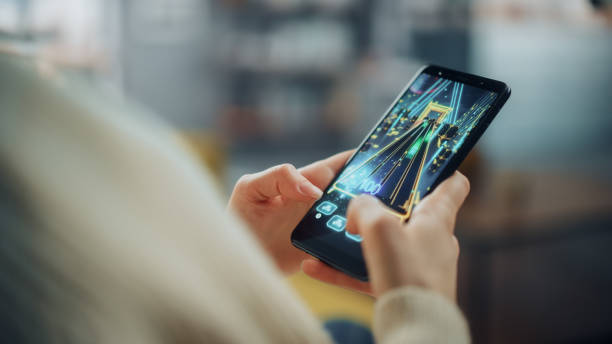 istock Close Up on a Person Hands Playing an Arcade Video Game on a Vertically Held Smartphone at Home Living Room. Feminine Hands Tapping the Mobile Phone Screen with a Colorful Game Over the Internet. 1324678088