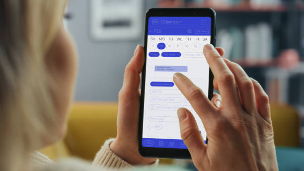 istock Beautiful Authentic Female Using a Smartphone with Calendar Application at Home Living Room while Lying on a Couch Sofa. She's Making Plans and Checking Event Schedule for a Day. 1324678107