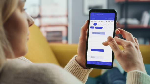 istock Beautiful Authentic Female Using a Smartphone with Calendar Application at Home Living Room while Lying on a Couch Sofa. She's Making Plans and Checking Event Schedule for a Day. 1324678185