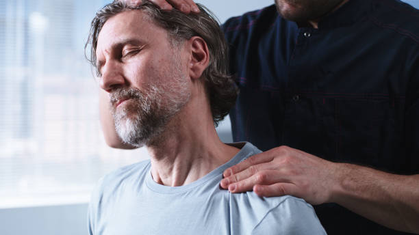 Crop therapist stretching neck of middle aged man Crop male therapist stretching neck of bearded mature man during rehabilitation session in clinic real time stock pictures, royalty-free photos & images
