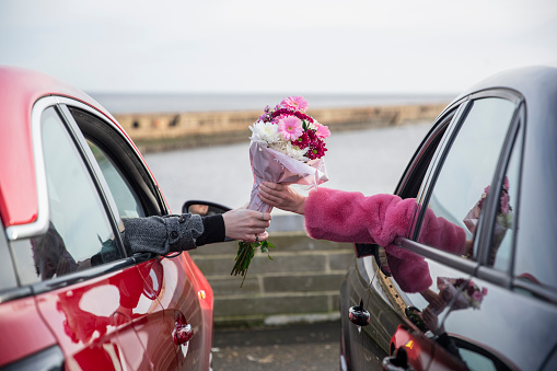 Unrecognisable couple handing a bunch of flowers between two cars in the North East of England during the Covid pandemic.