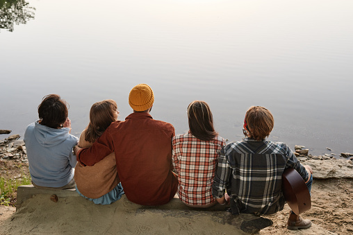 Rear view of friends sitting outdoors and enjoying the beautiful landscape of the lake