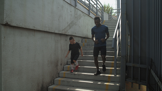 Pan left of black man and mixed race boy running on staircase during workout on stadium in summer