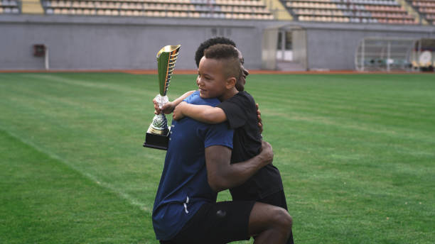 Black trainer giving cup to boy on football pitch African American man giving trophy and speaking with mixed race boy after football match on stadium real time stock pictures, royalty-free photos & images