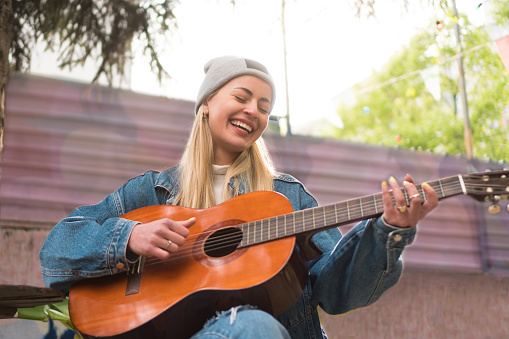 A beautiful teenage girl is playing acoustic guitar outdoors.