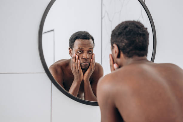istock African-American man looks in mirror making face in bathroom 1324687871
