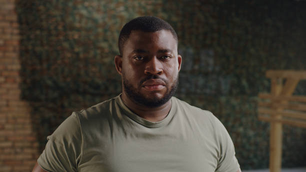 Serious male soldier looking at camera Bearded military man looking at camera with serious face against brick wall with USA flag on military base patriotic man stock pictures, royalty-free photos & images