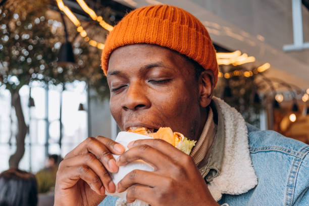 istock Pleasured African-America guy eats tasty hamburger in cafe 1324688095