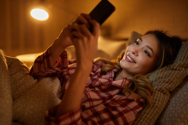 istock Beautiful young woman using mobile phone in bed at night 1324688102