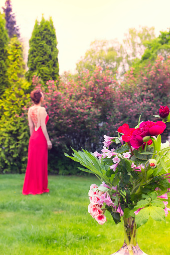 A bouquet of flowers in red tones on the background of a girl in a red dress. The bouquet consists of peonies, begonias, poppies and pink bells