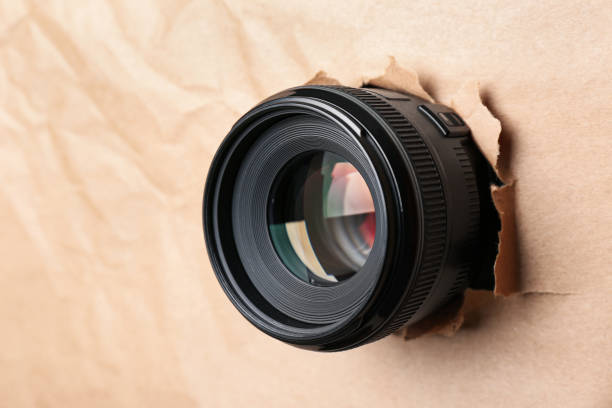 istock Hidden camera lens through hole in paper, closeup 1324692768
