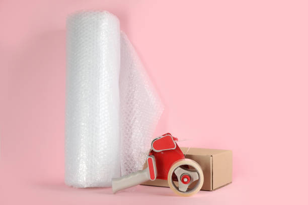 istock bubble pack roll, tape dispenser and cardboard box on pink background, space for text 1324693051