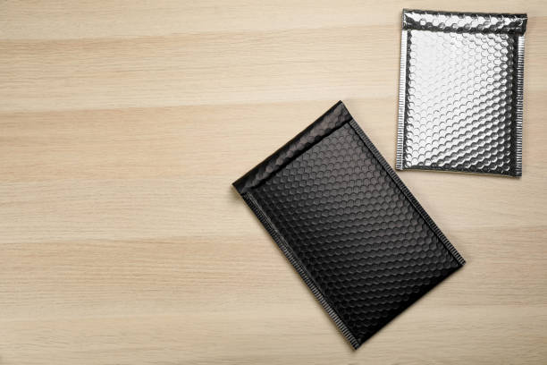 Two padded envelopes with bubble pack on wooden background, flat lay. Space for text