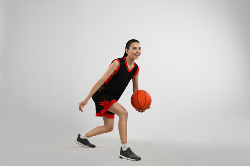 Professional sportswoman playing basketball on grey background