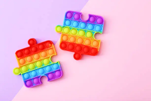Photo of Popit toy in the form of a puzzles on a colorful background. Multicolored Pop it toy