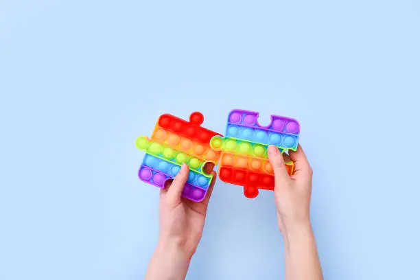 Photo of Popit toys in the form of puzzles in hands on a blue background. Multicolored Pop it toy