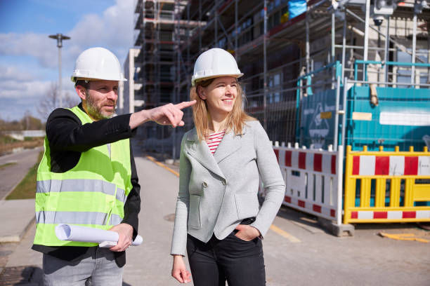 istock An architect or civil engineer with planning documents meets with a customer or colleague on the large construction site and both of them wear white protective helmets. 1324696757