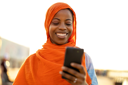 Beautiful, happy Muslim woman using smartphone outdoors
